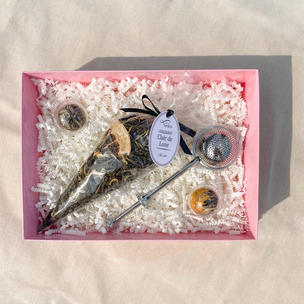 Drobny upominek z herbatą premium, dwiema herbatami rozkwitającymi i metalowym zaparzaczem