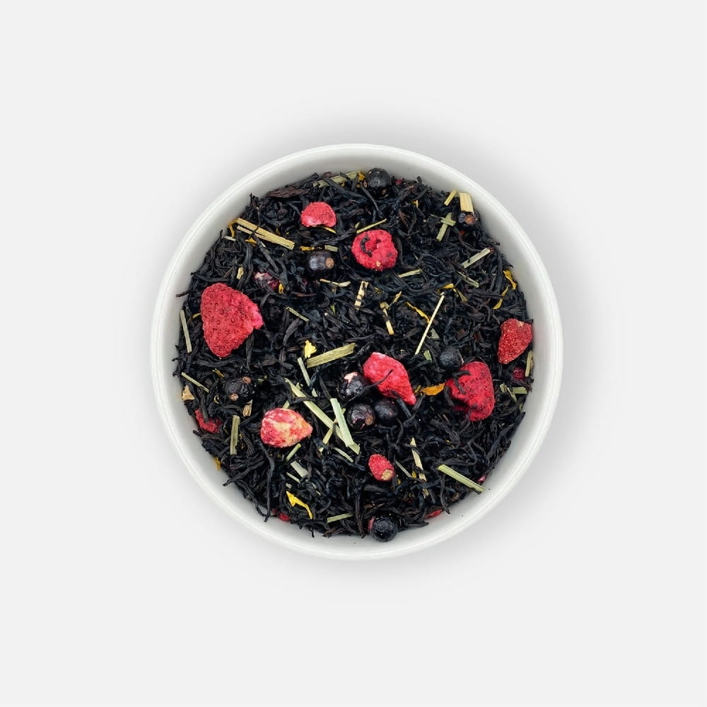 Czarna herbata liściasta Sun-Kissed Meadow z liofilizowanymi owocami porzeczki, malin, poziomek, trawą cytrynową i płatkami kwiatu słonecznika, podana w białej miseczce, ujęcie z góry.