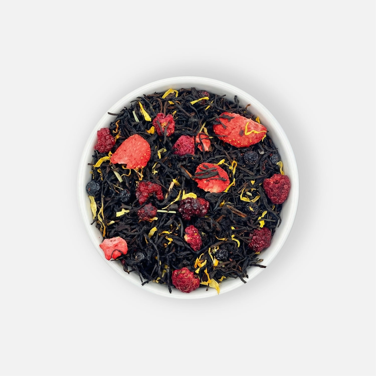 Czarna herbata liściasta Berry Belle z liofilizowaną truskawką, maliną, jeżyną i jagodą, trawą cytrynową oraz kwiatem nagietka, podana w białej miseczce, ujęcie z góry.