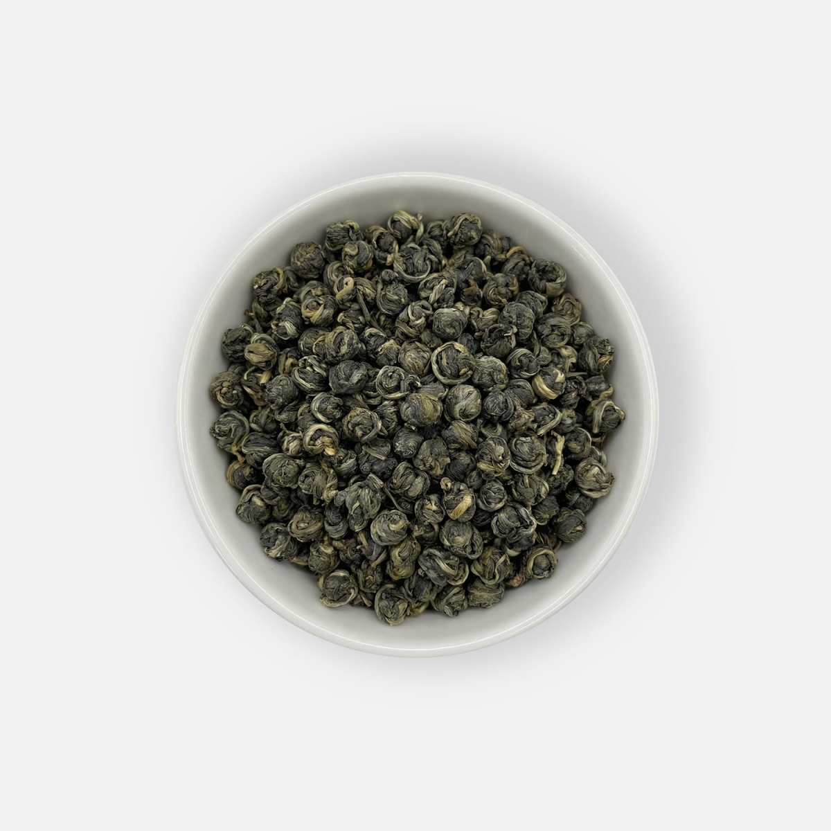 Zielona herbata liściasta Long Zhu Jasmine zwijana w perły, z dodatkiem kwiatu jaśminu, podana w białej miseczce, ujęcie z góry.