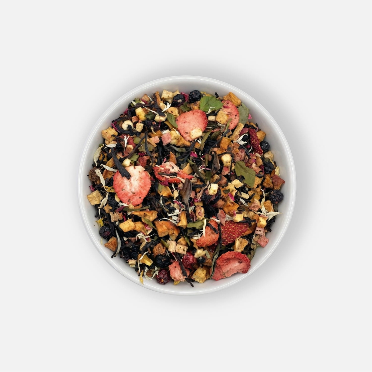 Herbata Secret Garden z suszonymi i liofilizowanymi owocami, czarną i białą herbatą oraz kwiatem bławatka, podana w białej miseczce, ujęcie z góry.