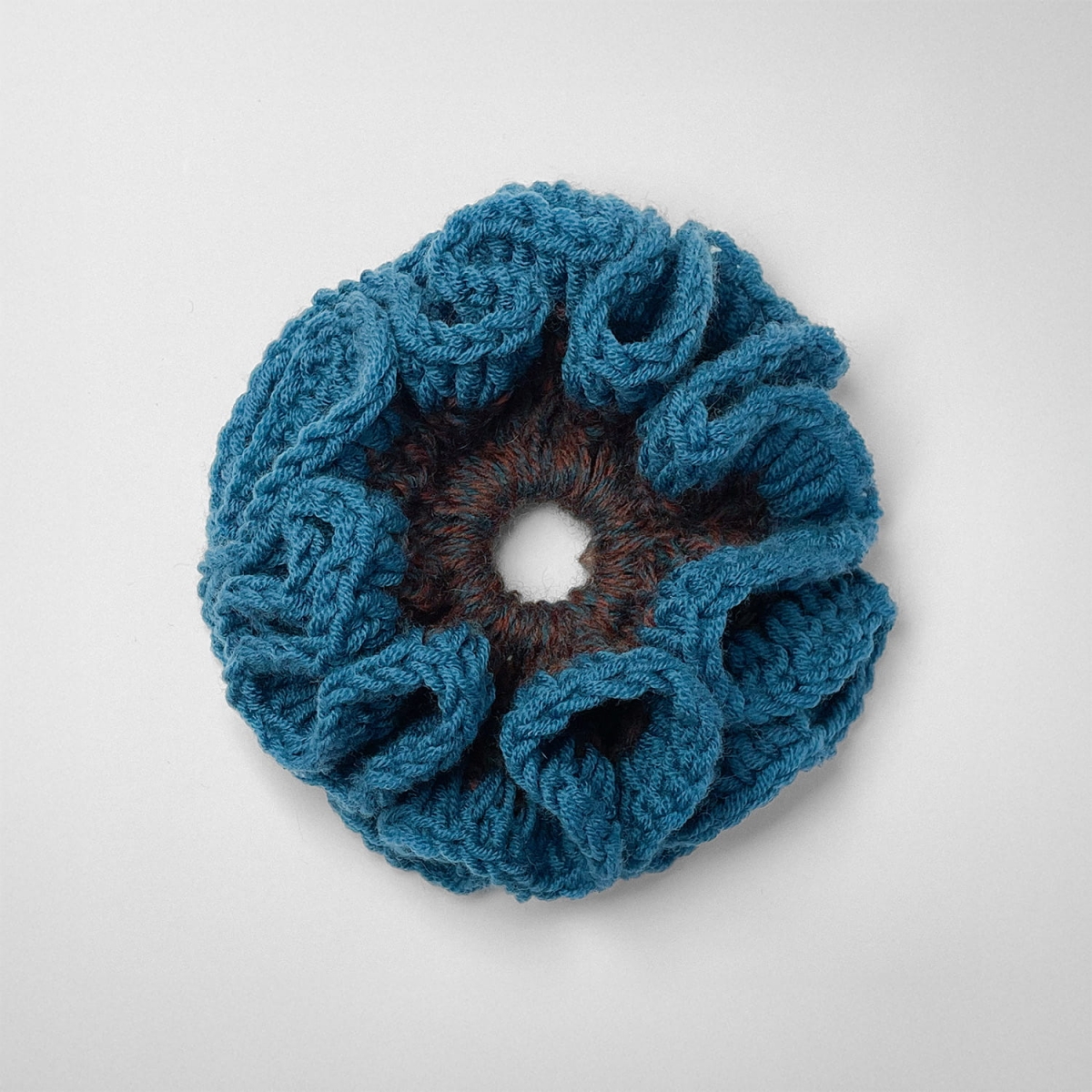 Ręcznie robiona gumka do włosów na szydełku wykonana z materiałów z upcyklingu, widok z góry na białym tle.