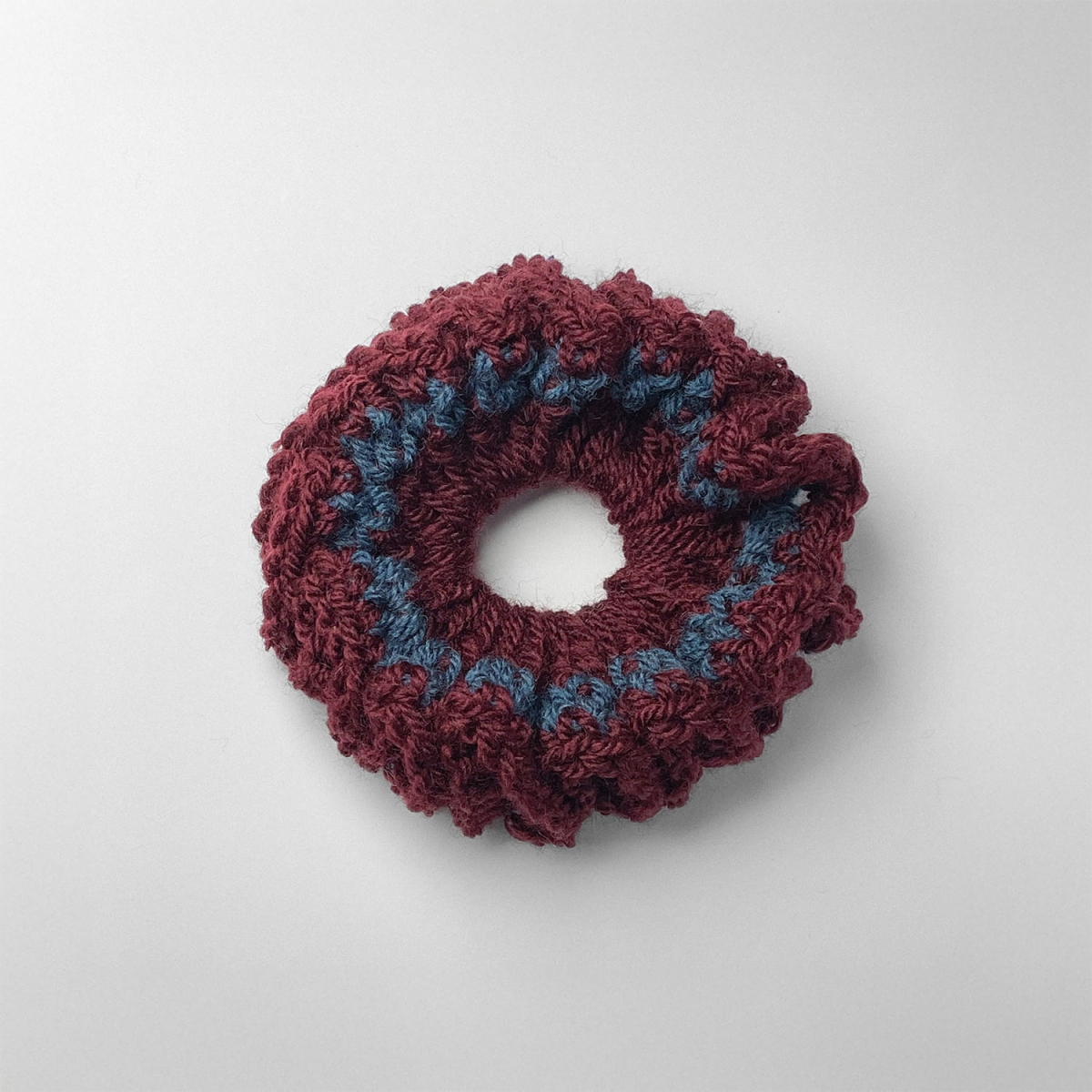 Ręcznie robiona gumka do włosów na szydełku wykonana z materiałów z upcyklingu, widok z góry na białym tle.