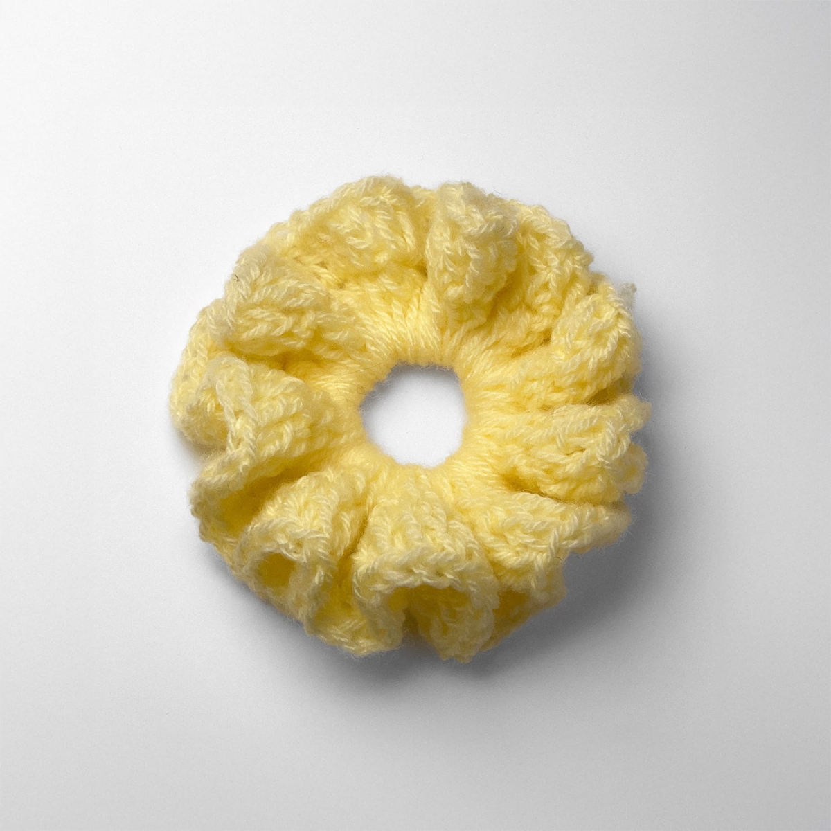 Ręcznie robiona gumka do włosów na szydełku wykonana z materiałów z upcyklingu, widok z góry na białym tle.