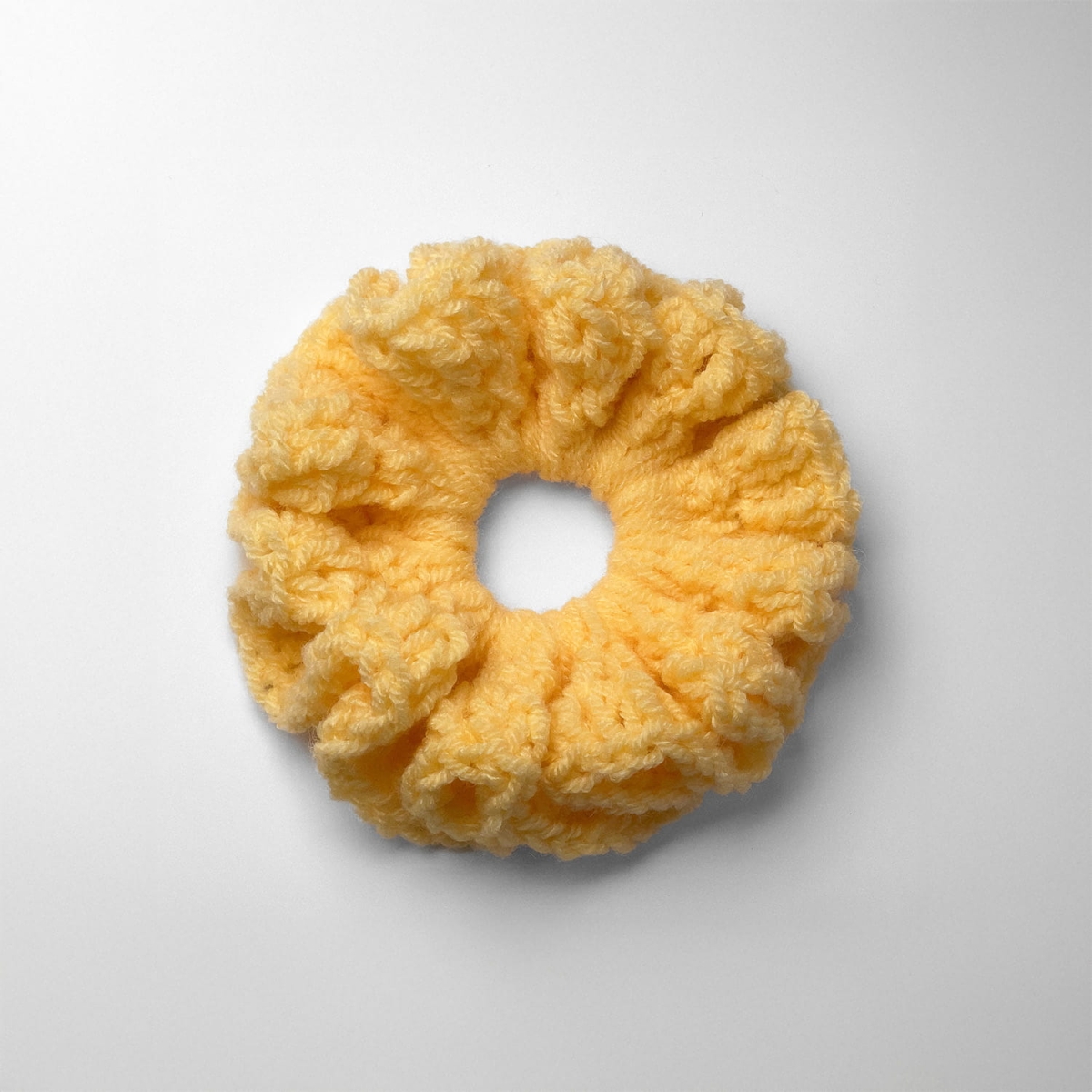 Ręcznie robiona gumka do włosów na szydełku wykonana z materiałów z upcyklingu, widok z góry na białym tle.