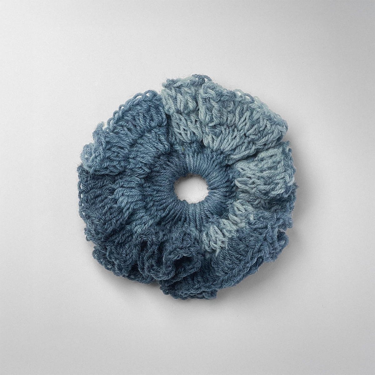 Ręcznie robiona gumka do włosów na szydełku wykonana z materiałów z upcyklingu, widok z góry na białym tle.