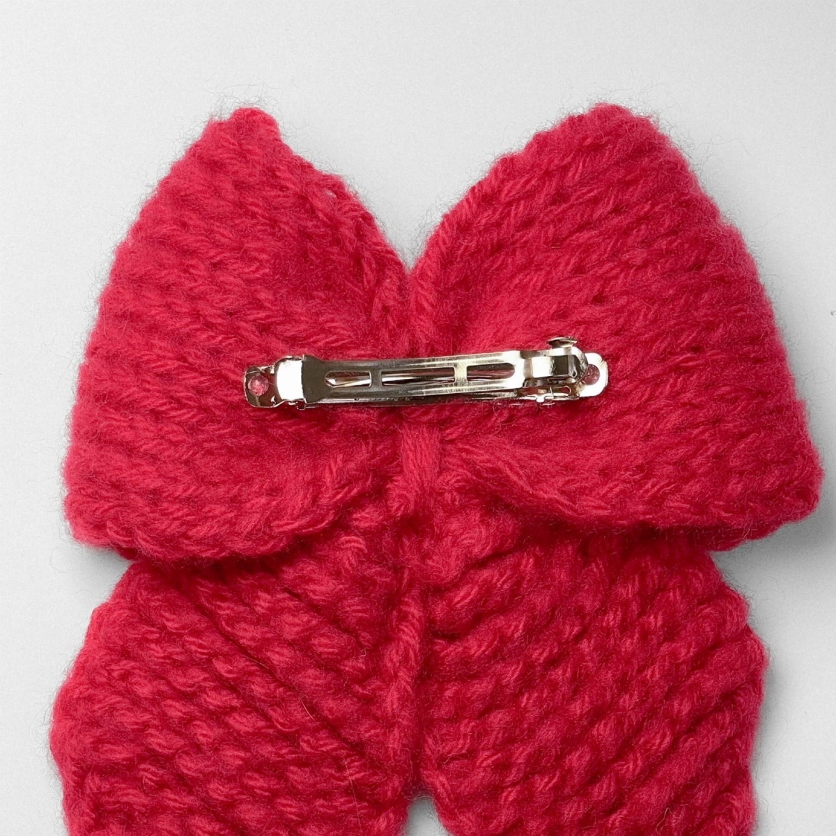 Ręcznie dziergana spinka do włosów w formie kokardy, widok z góry na jasnym tle.