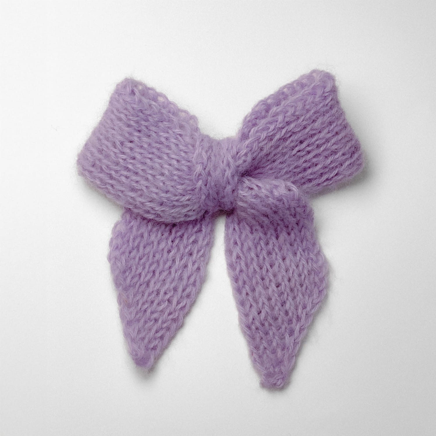 Ręcznie dziergana spinka do włosów w formie kokardy, widok z góry na jasnym tle.