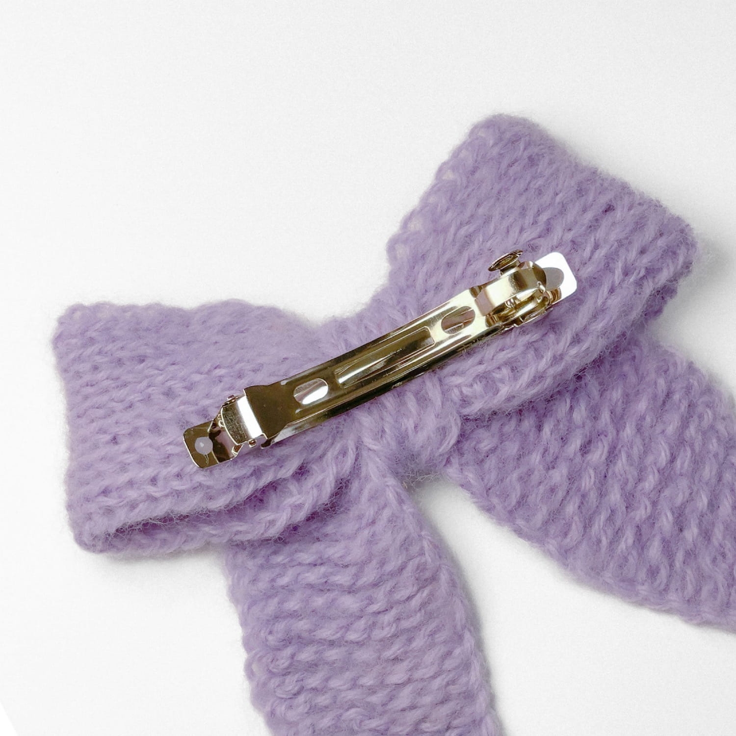 Ręcznie dziergana spinka do włosów w formie kokardy, widok z góry na jasnym tle.