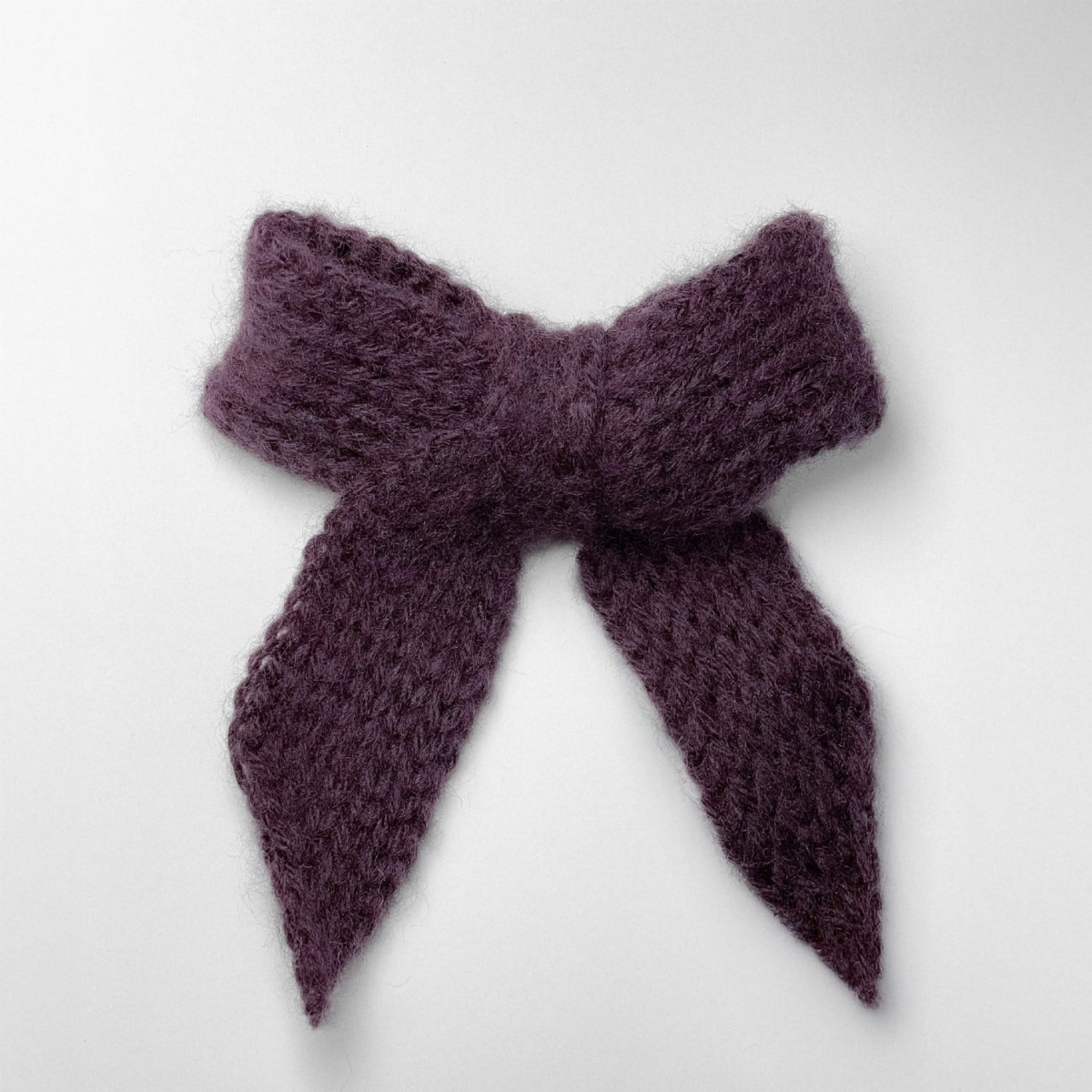 Ręcznie dziergana spinka do włosów w formie kokardy, widok z góry na jasnym tle.