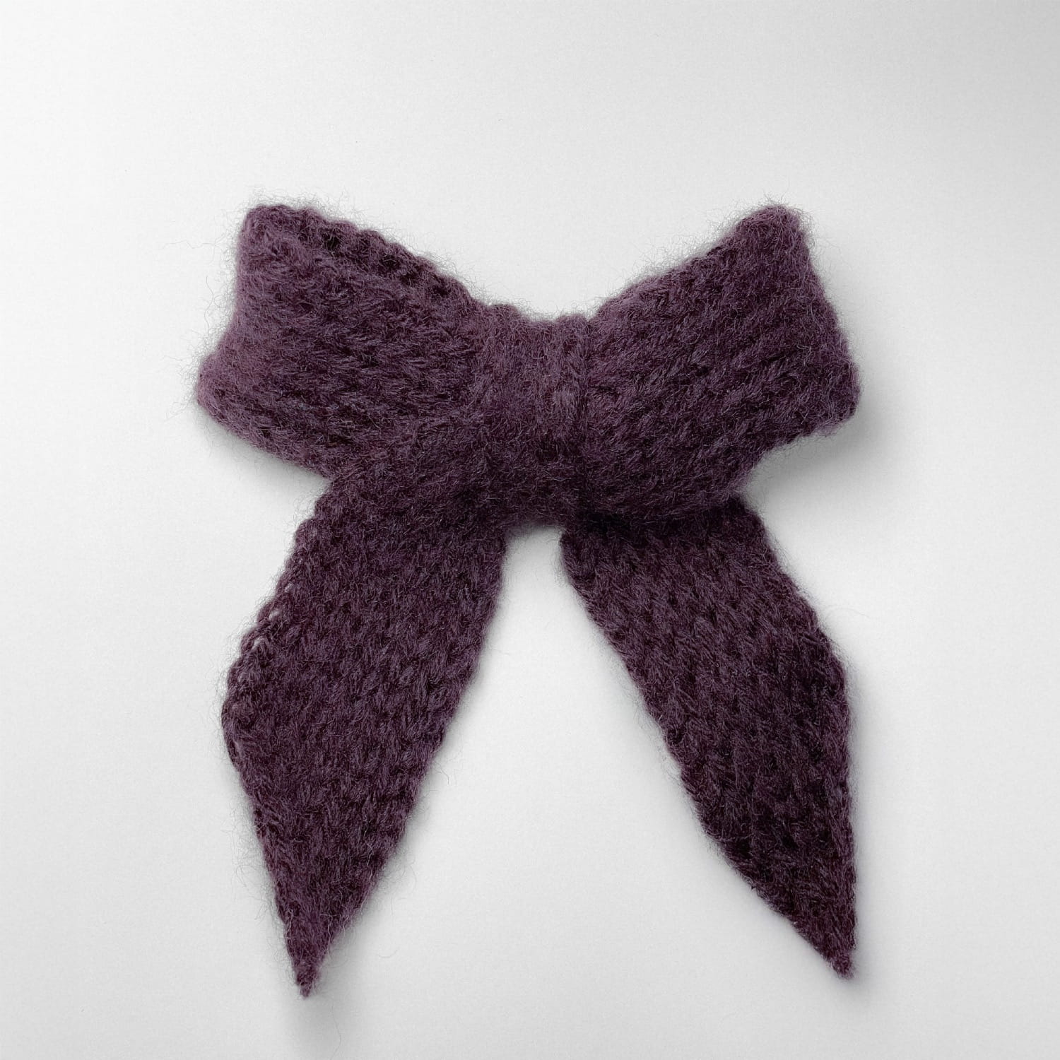 Ręcznie dziergana spinka do włosów w formie kokardy, widok z góry na jasnym tle.