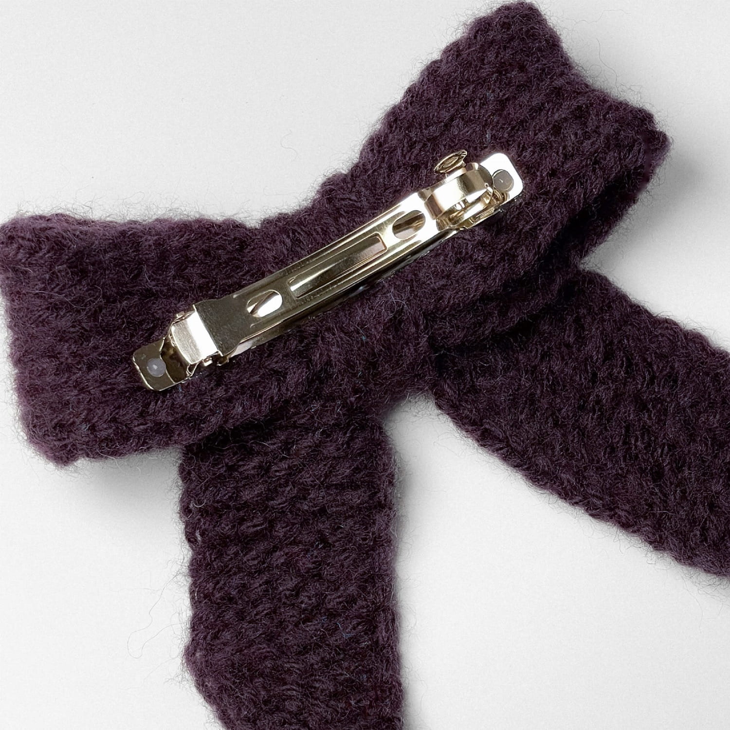 Ręcznie dziergana spinka do włosów w formie kokardy, widok z góry na jasnym tle.