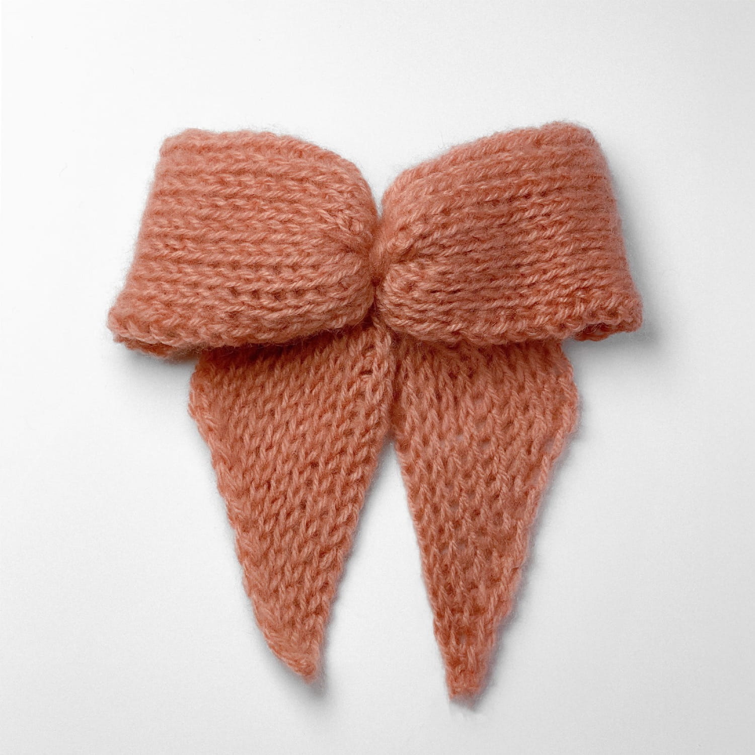 Ręcznie dziergana spinka do włosów w formie kokardy, widok z góry na jasnym tle.