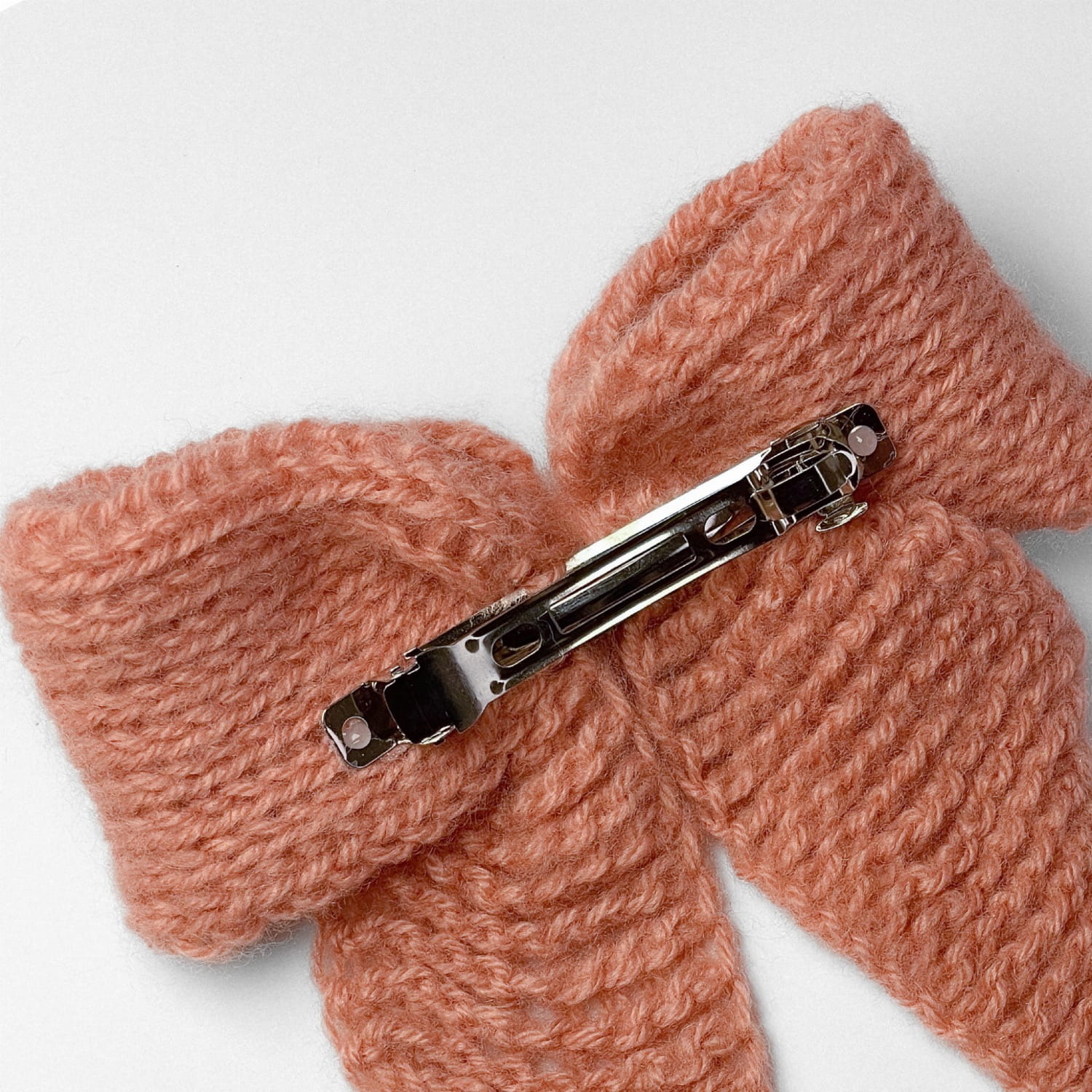 Ręcznie dziergana spinka do włosów w formie kokardy, widok z góry na jasnym tle.