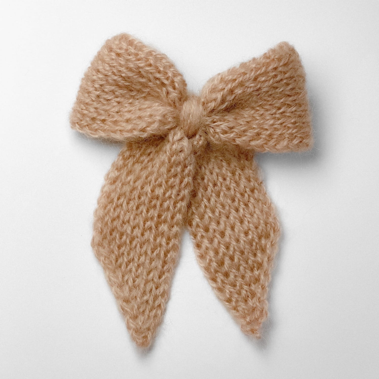 Ręcznie dziergana spinka do włosów w formie kokardy, widok z góry na jasnym tle.