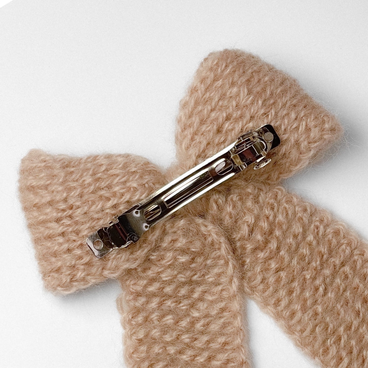 Ręcznie dziergana spinka do włosów w formie kokardy, widok z góry na jasnym tle.