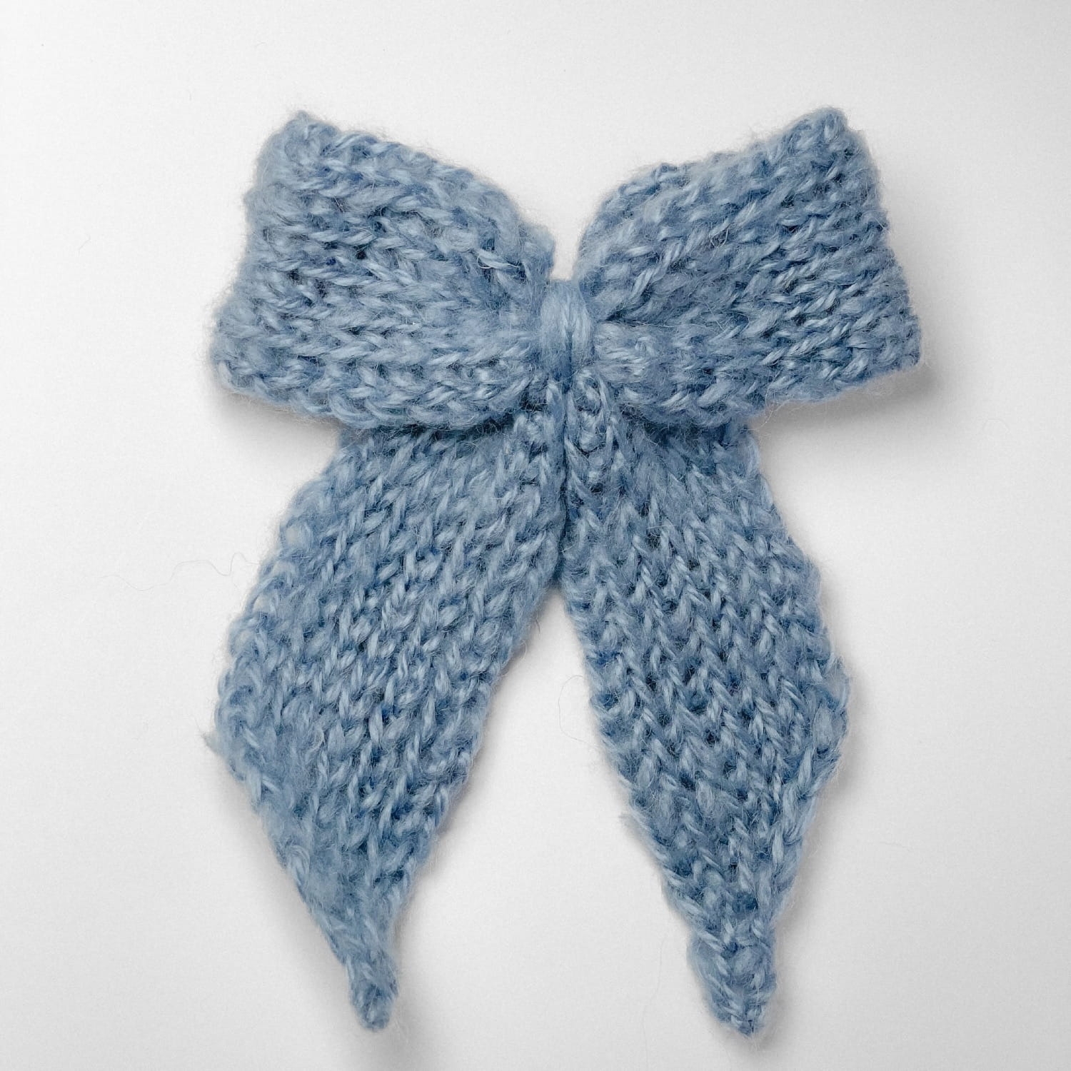 Ręcznie dziergana spinka do włosów w formie kokardy, widok z góry na jasnym tle.