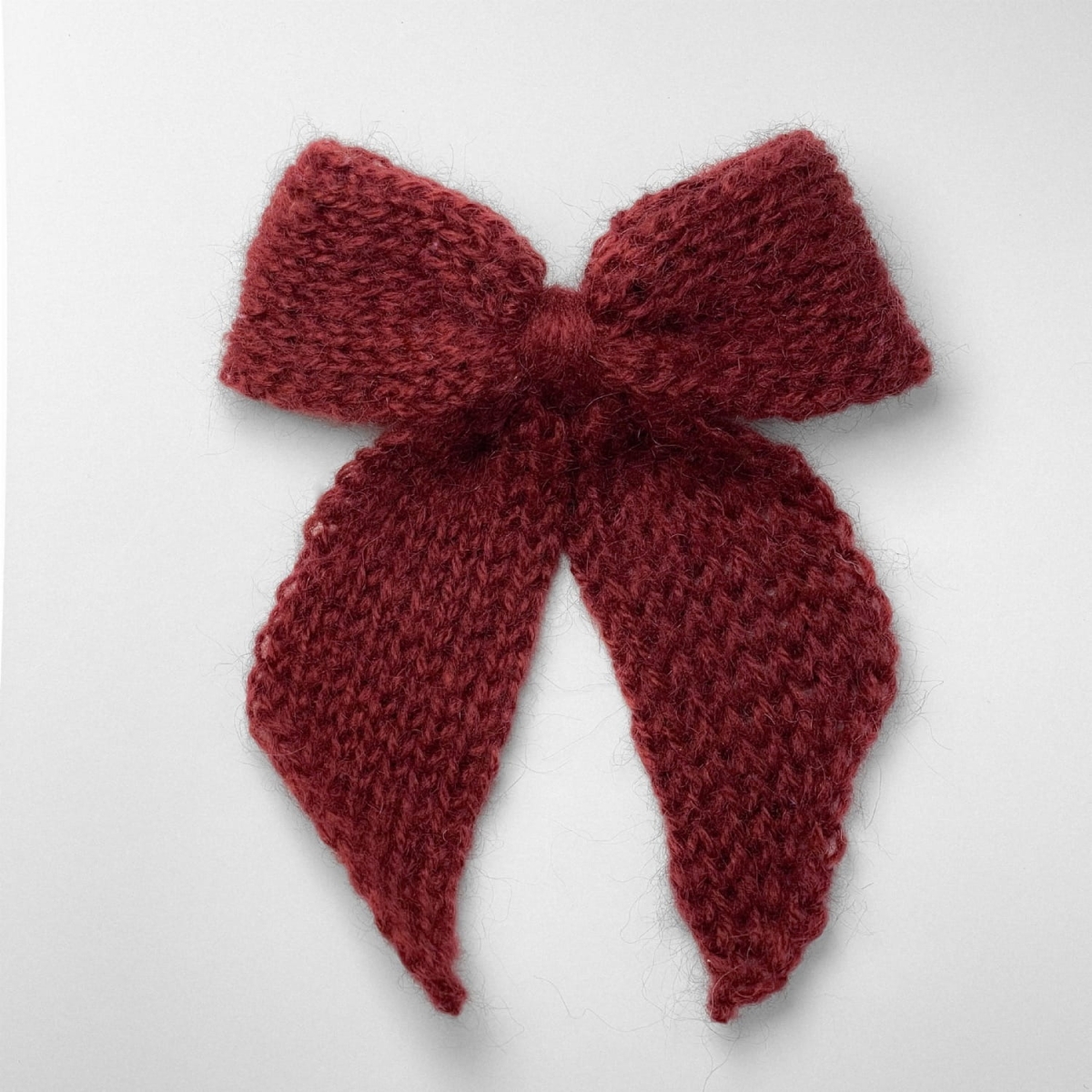 Ręcznie dziergana spinka do włosów w formie kokardy, widok z góry na jasnym tle.