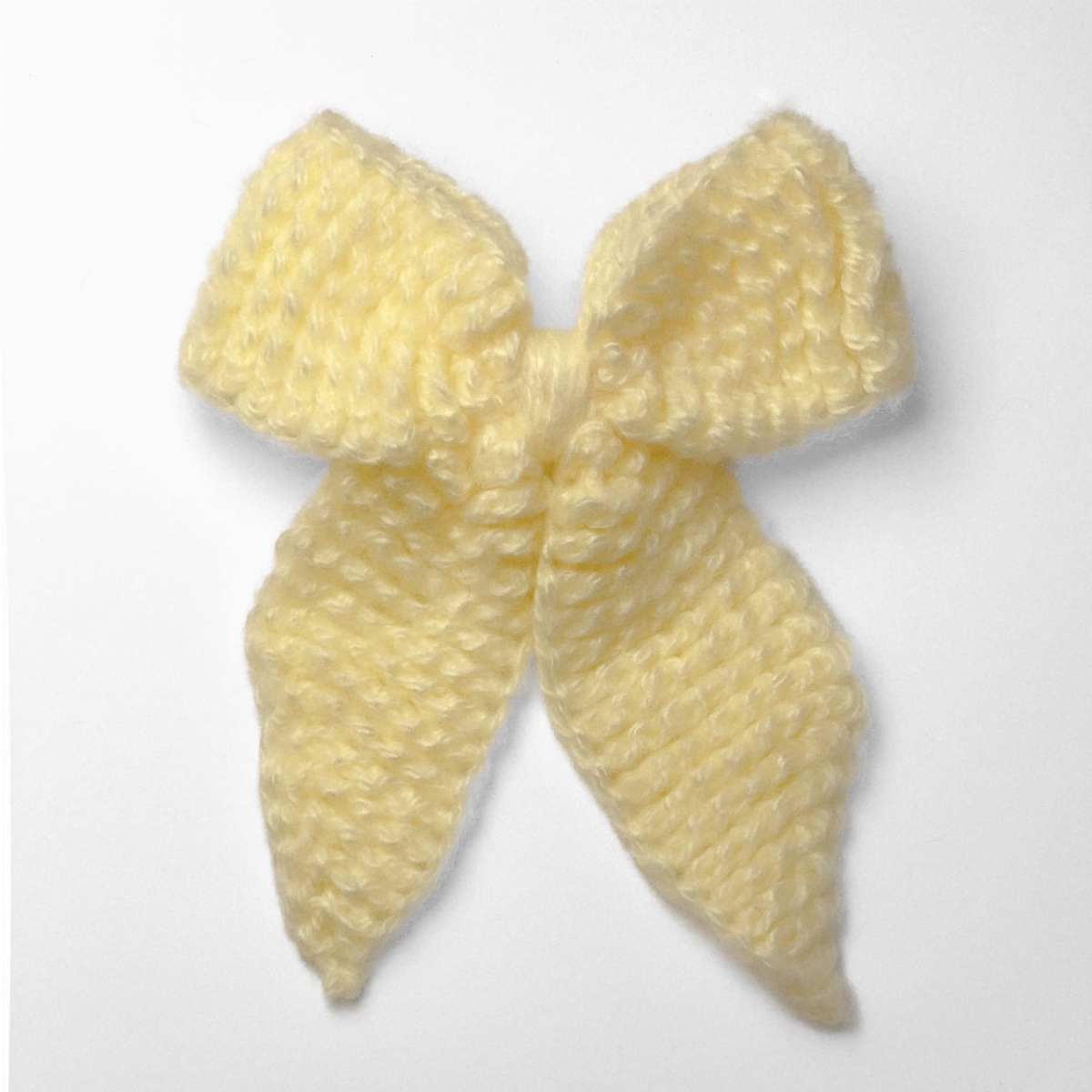 Ręcznie dziergana spinka do włosów w formie kokardy, widok z góry na jasnym tle.