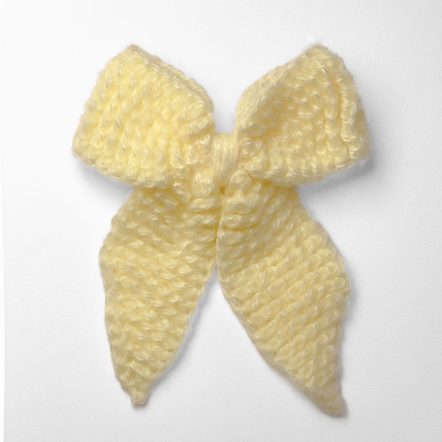 Ręcznie dziergana spinka do włosów w formie kokardy, widok z góry na jasnym tle.