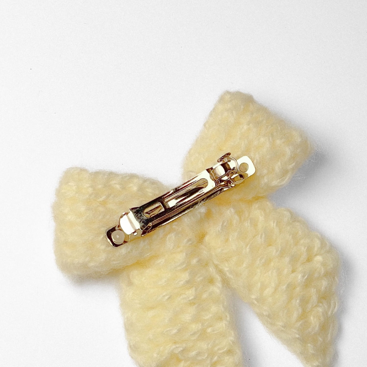 Ręcznie dziergana spinka do włosów w formie kokardy, widok z góry na jasnym tle.