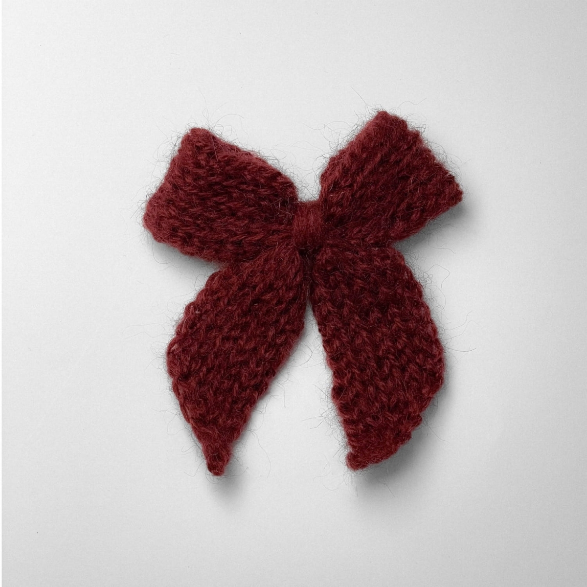 Ręcznie dziergana spinka do włosów w formie kokardy, widok z góry na jasnym tle.