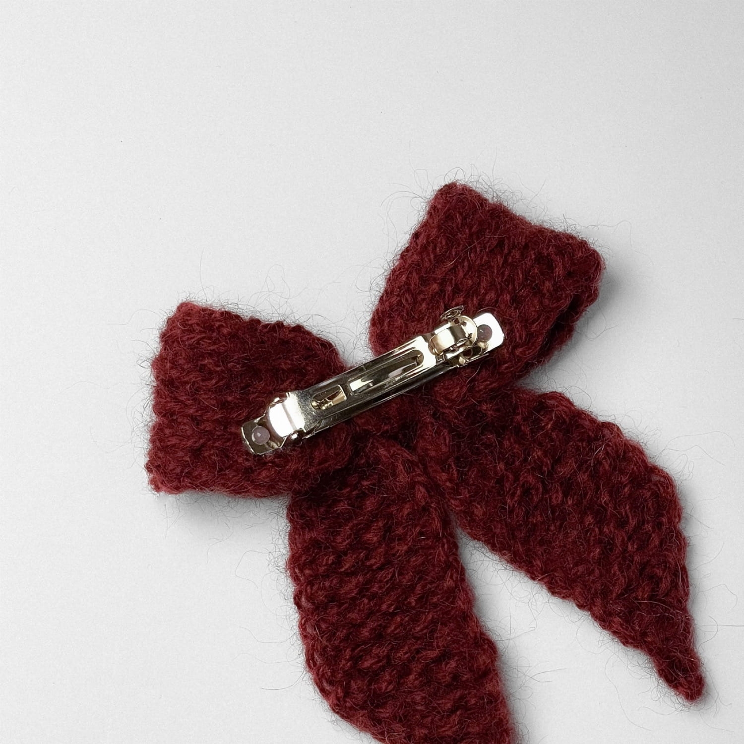 Ręcznie dziergana spinka do włosów w formie kokardy, widok z góry na jasnym tle.