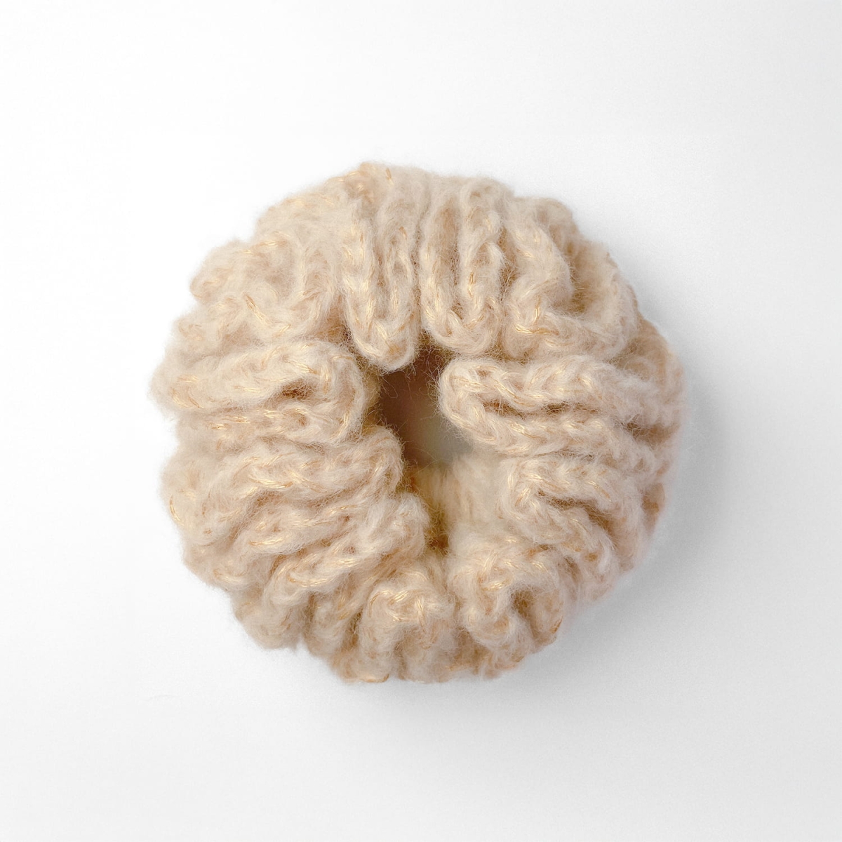 Ręcznie robiona, złota, puchata  gumka do włosów na szydełku wykonana z materiałów z upcyklingu, widok z góry na białym tle.