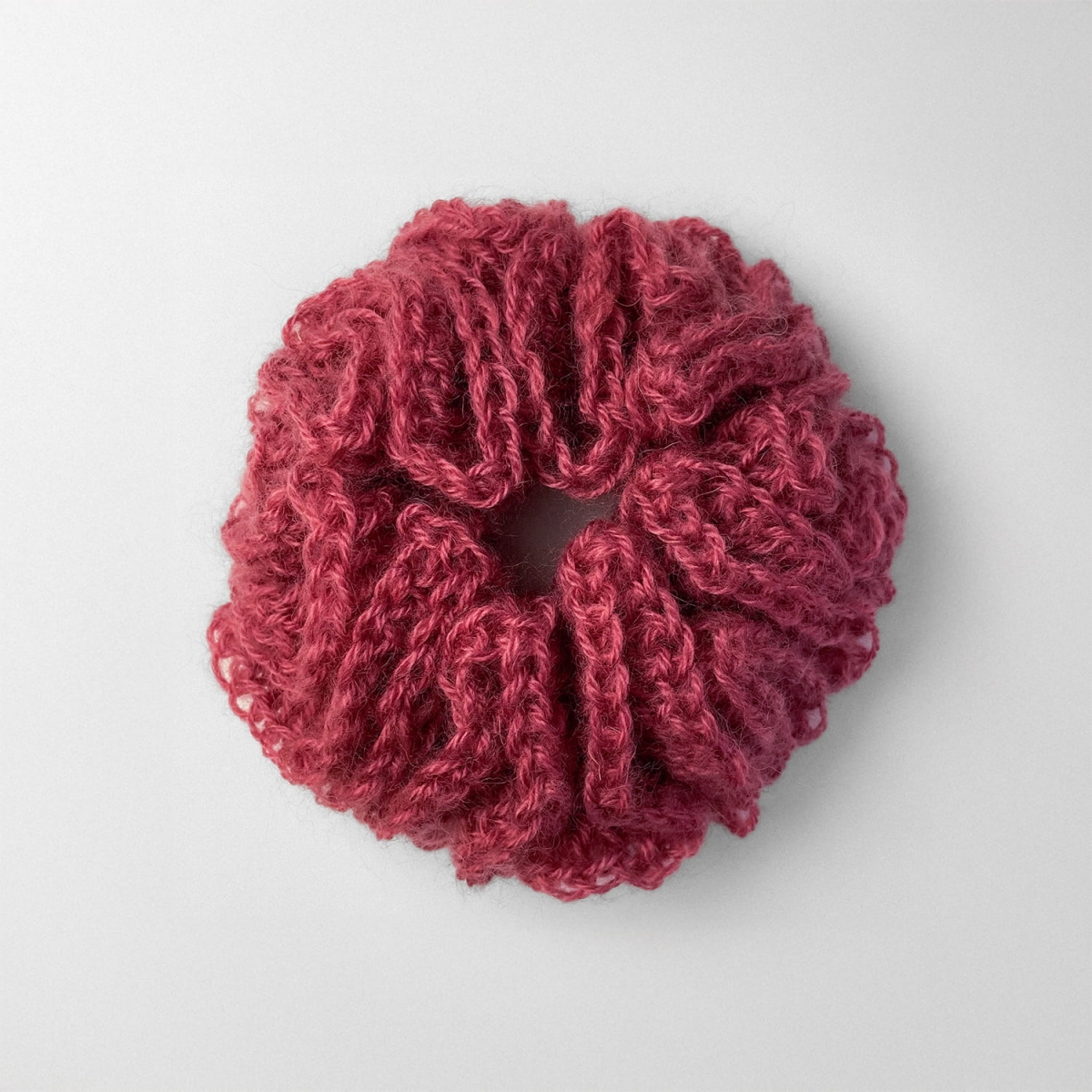 Ręcznie robiona, puchata  gumka do włosów na szydełku wykonana z materiałów z upcyklingu, widok z góry na białym tle.