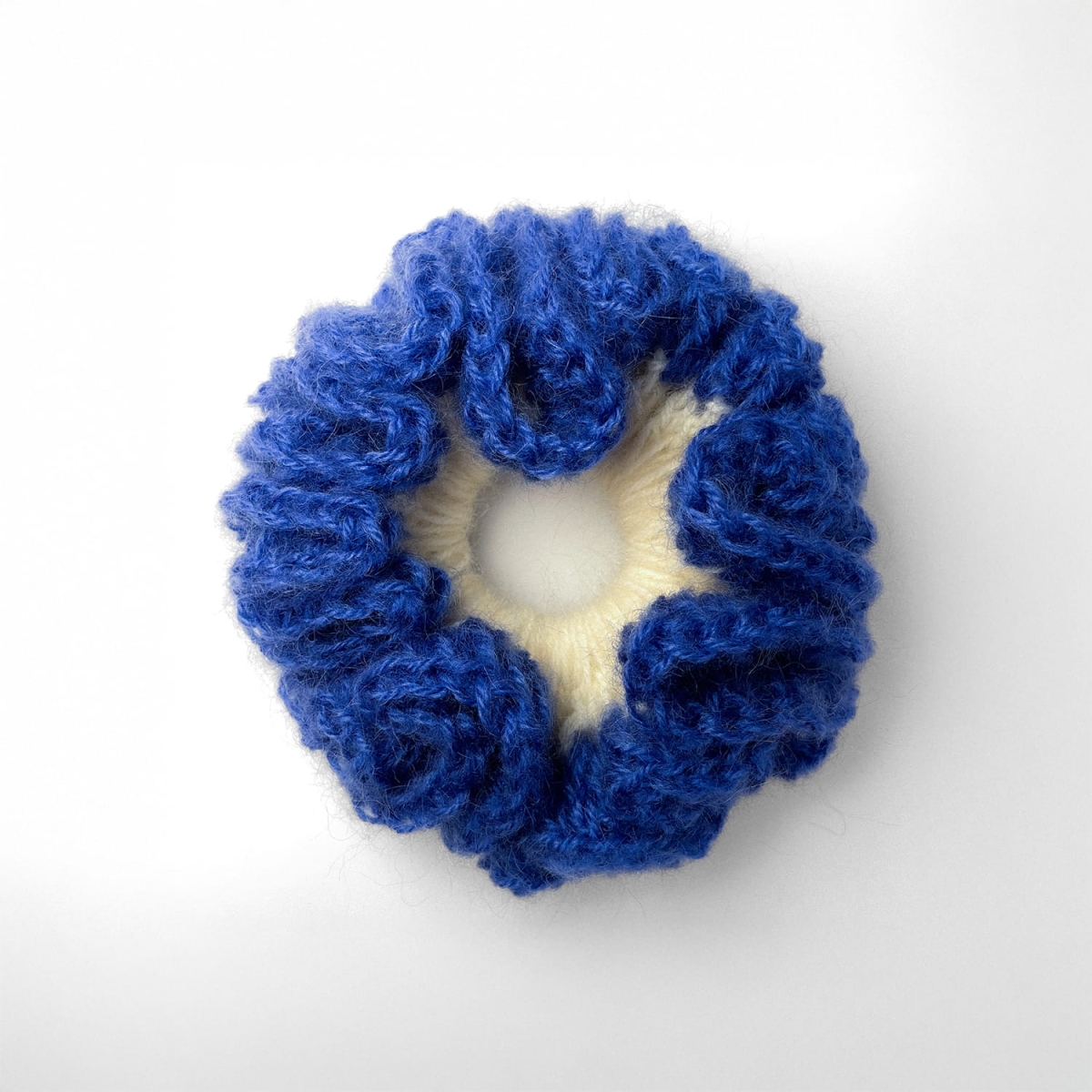 Ręcznie robiona, puchata  gumka do włosów na szydełku wykonana z materiałów z upcyklingu, widok z góry na białym tle.