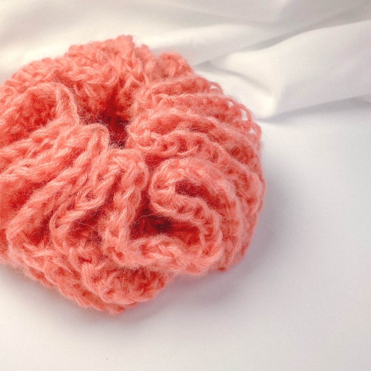 Ręcznie robiona, puchata  gumka do włosów na szydełku wykonana z materiałów z upcyklingu, widok z góry na białym tle.