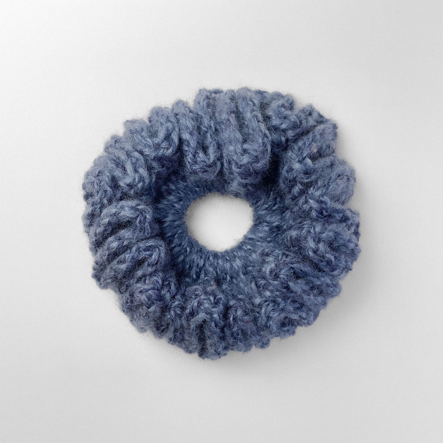 Ręcznie robiona, puchata  gumka do włosów na szydełku wykonana z materiałów z upcyklingu, widok z góry na białym tle.