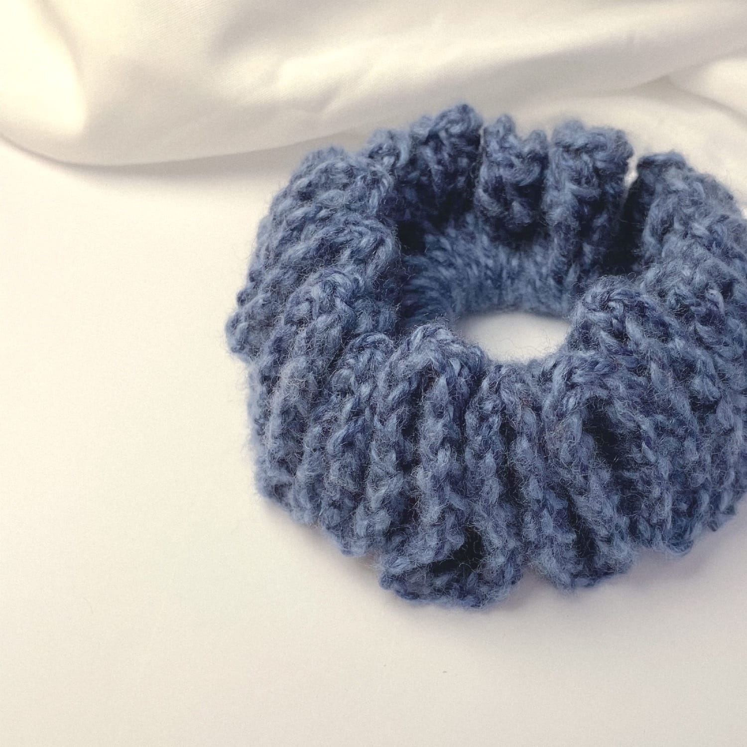 Ręcznie robiona, puchata  gumka do włosów na szydełku wykonana z materiałów z upcyklingu, widok z góry na białym tle.
