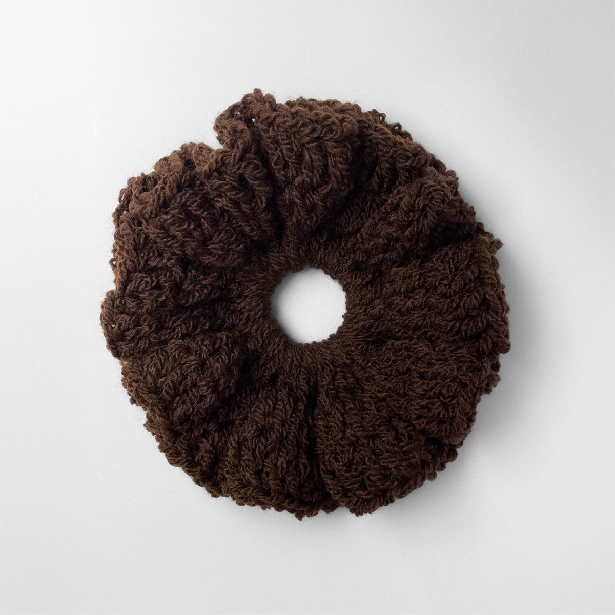 Ręcznie robiona, puchata  gumka do włosów na szydełku wykonana z materiałów z upcyklingu, widok z góry na białym tle.