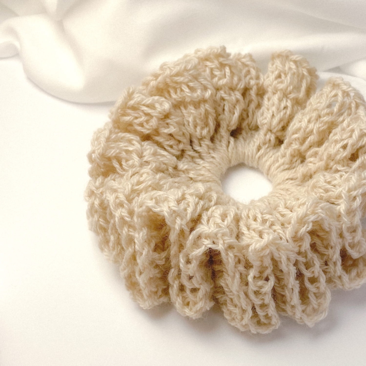 Ręcznie robiona, puchata  gumka do włosów na szydełku wykonana z materiałów z upcyklingu, widok z góry na białym tle.