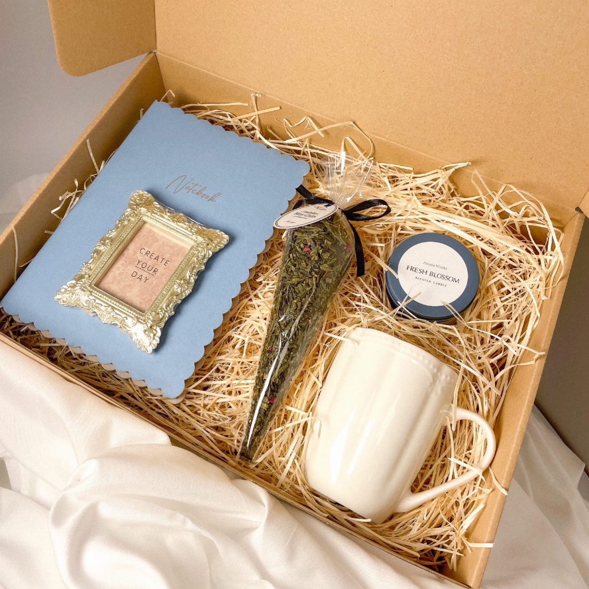 Zestaw prezentowy z niebieskim notesem, herbatą, świeczką i wiosennym kubkiem.