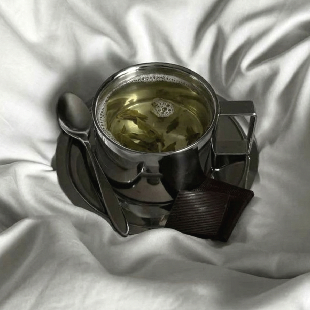 Metalowa filiżanka z łyżeczką na białej pościeli.