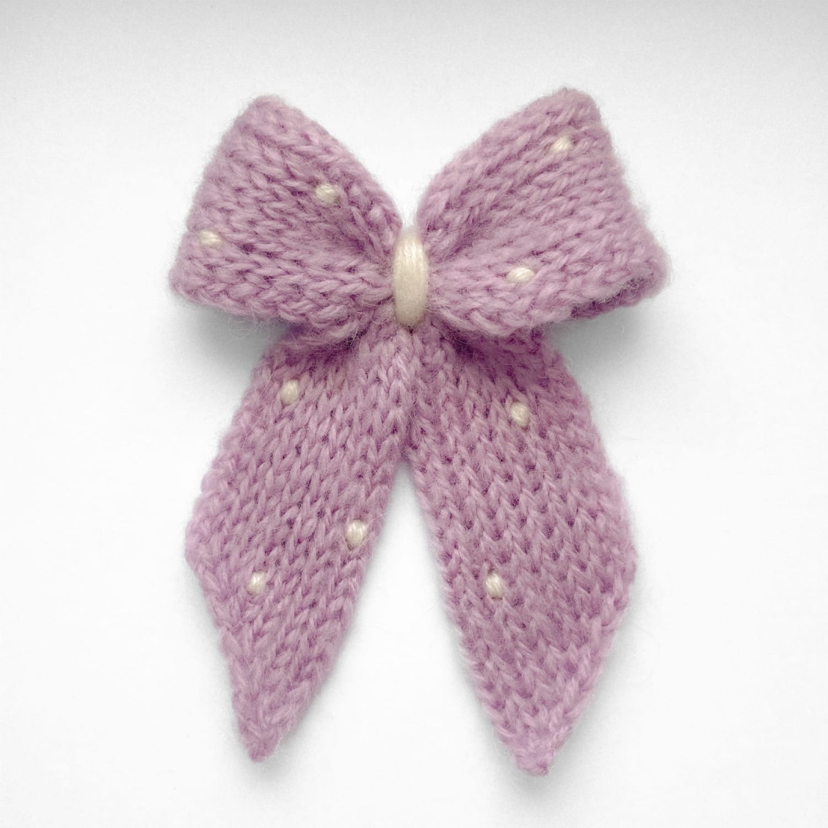 Ręcznie dziergana spinka do włosów w formie kokardy, widok z góry na jasnym tle.