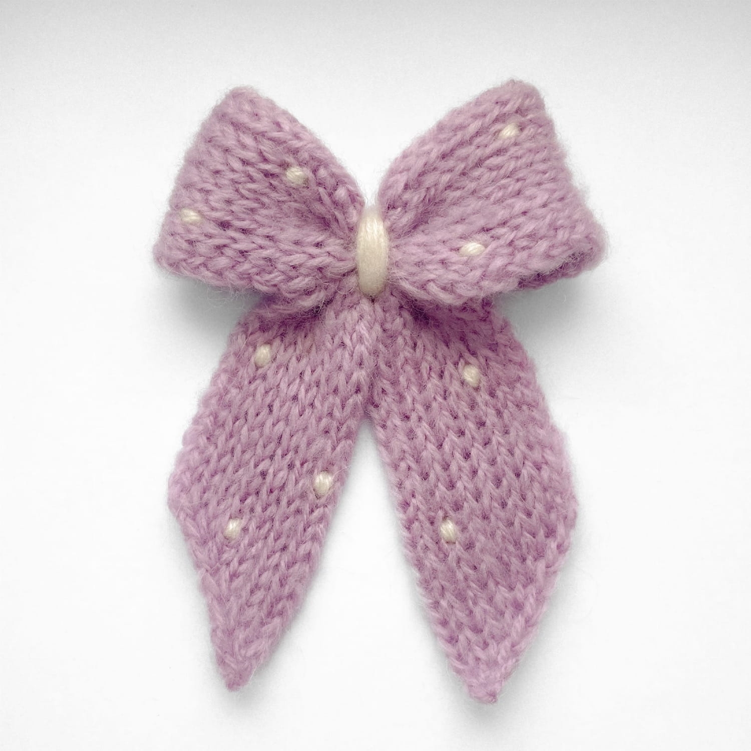 Ręcznie dziergana spinka do włosów w formie kokardy, widok z góry na jasnym tle.