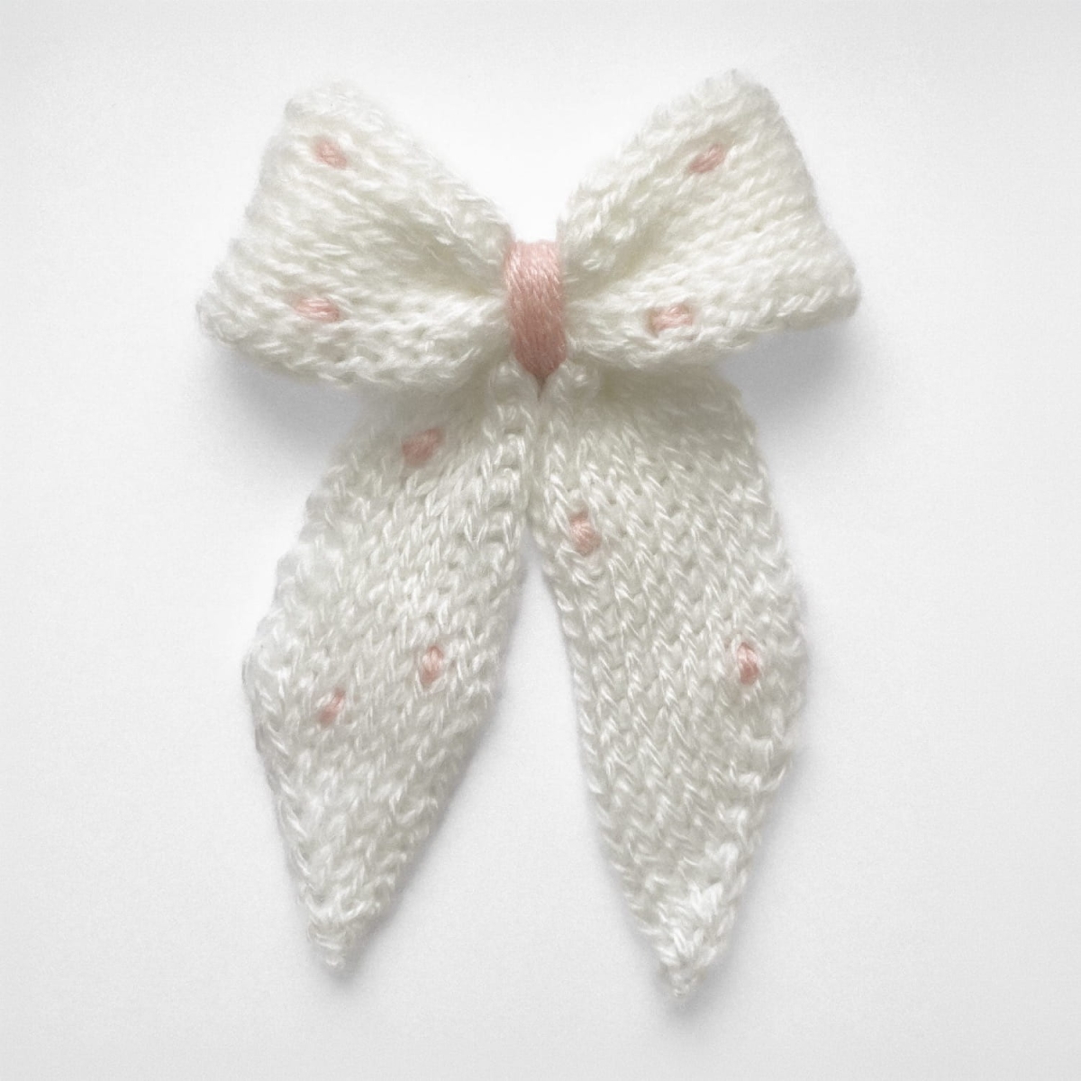 Ręcznie dziergana spinka do włosów w formie kokardy, widok z góry na jasnym tle.