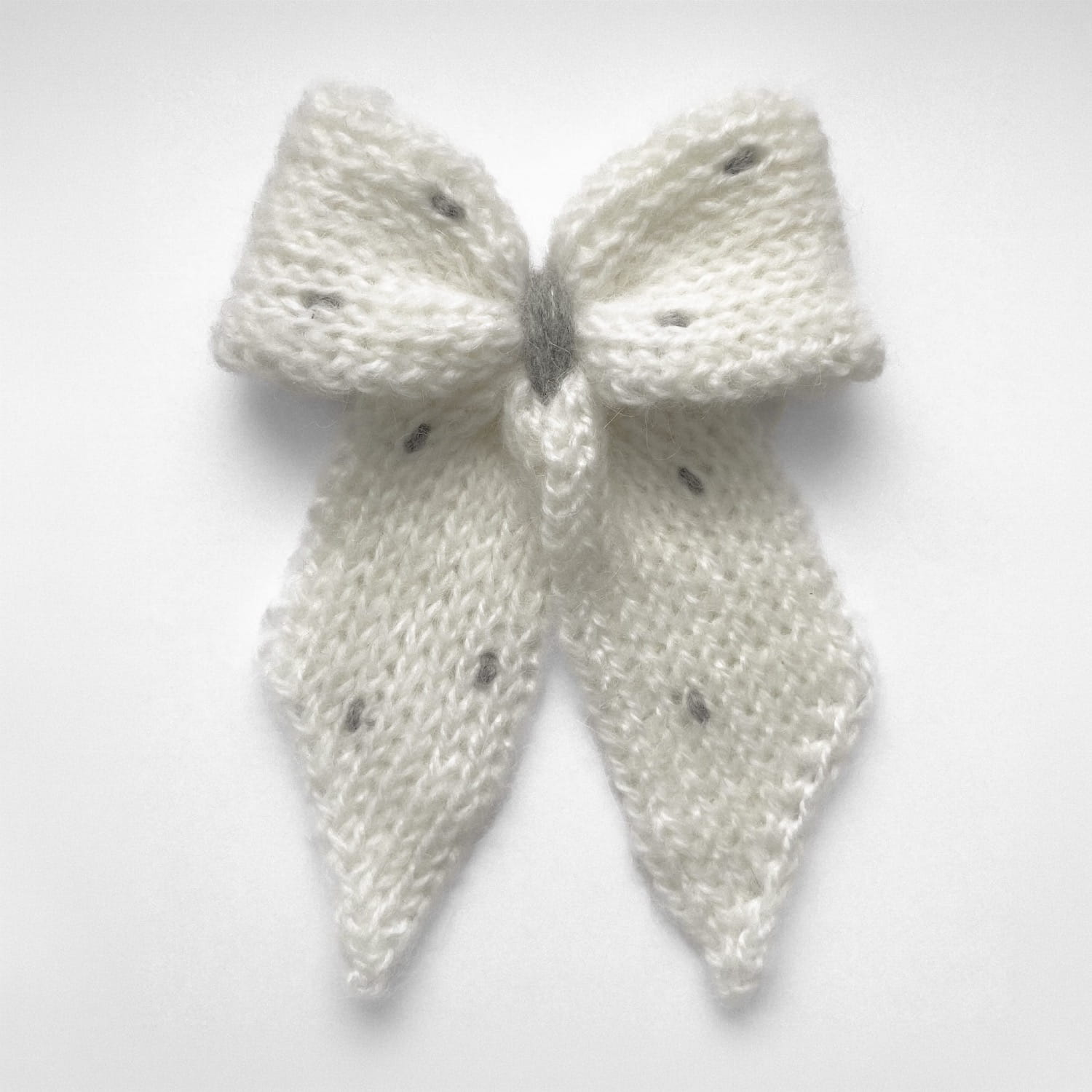 Ręcznie dziergana spinka do włosów w formie kokardy, widok z góry na jasnym tle.