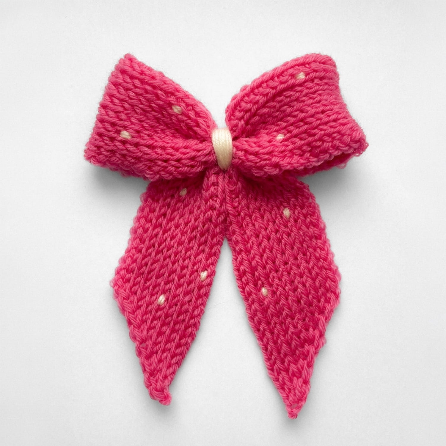 Ręcznie dziergana spinka do włosów w formie kokardy, widok z góry na jasnym tle.