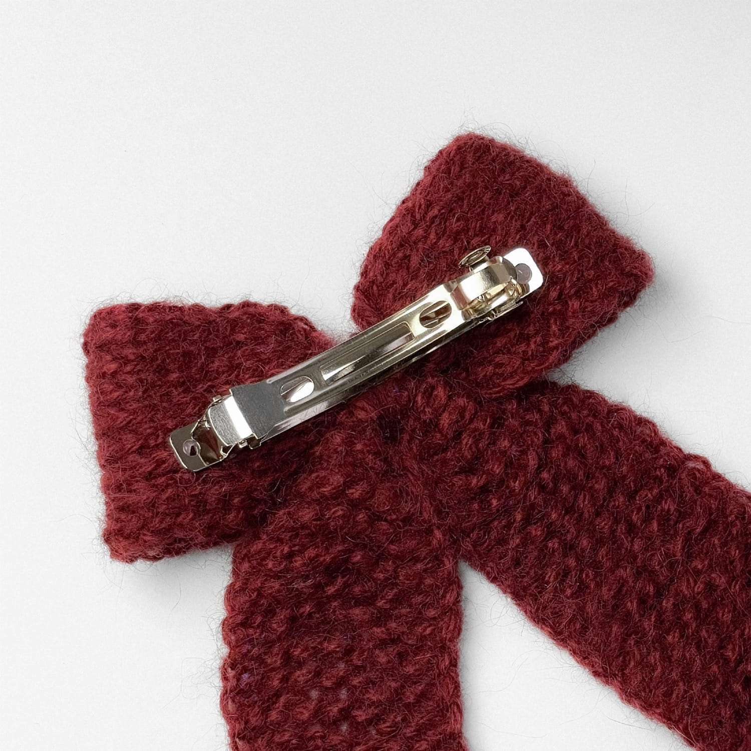 Ręcznie dziergana spinka do włosów w formie kokardy, widok z góry na jasnym tle.