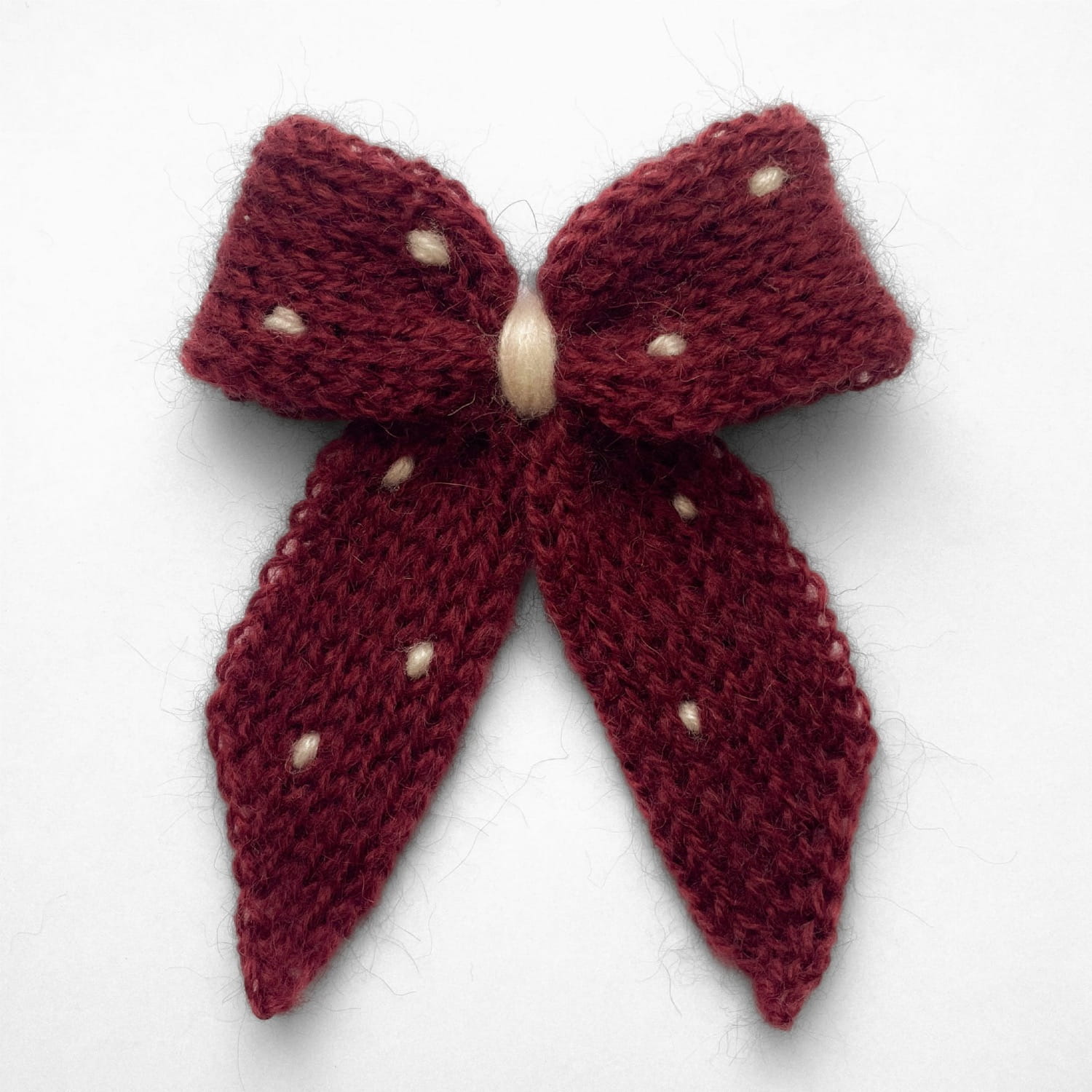 Ręcznie dziergana spinka do włosów w formie kokardy, widok z góry na jasnym tle.