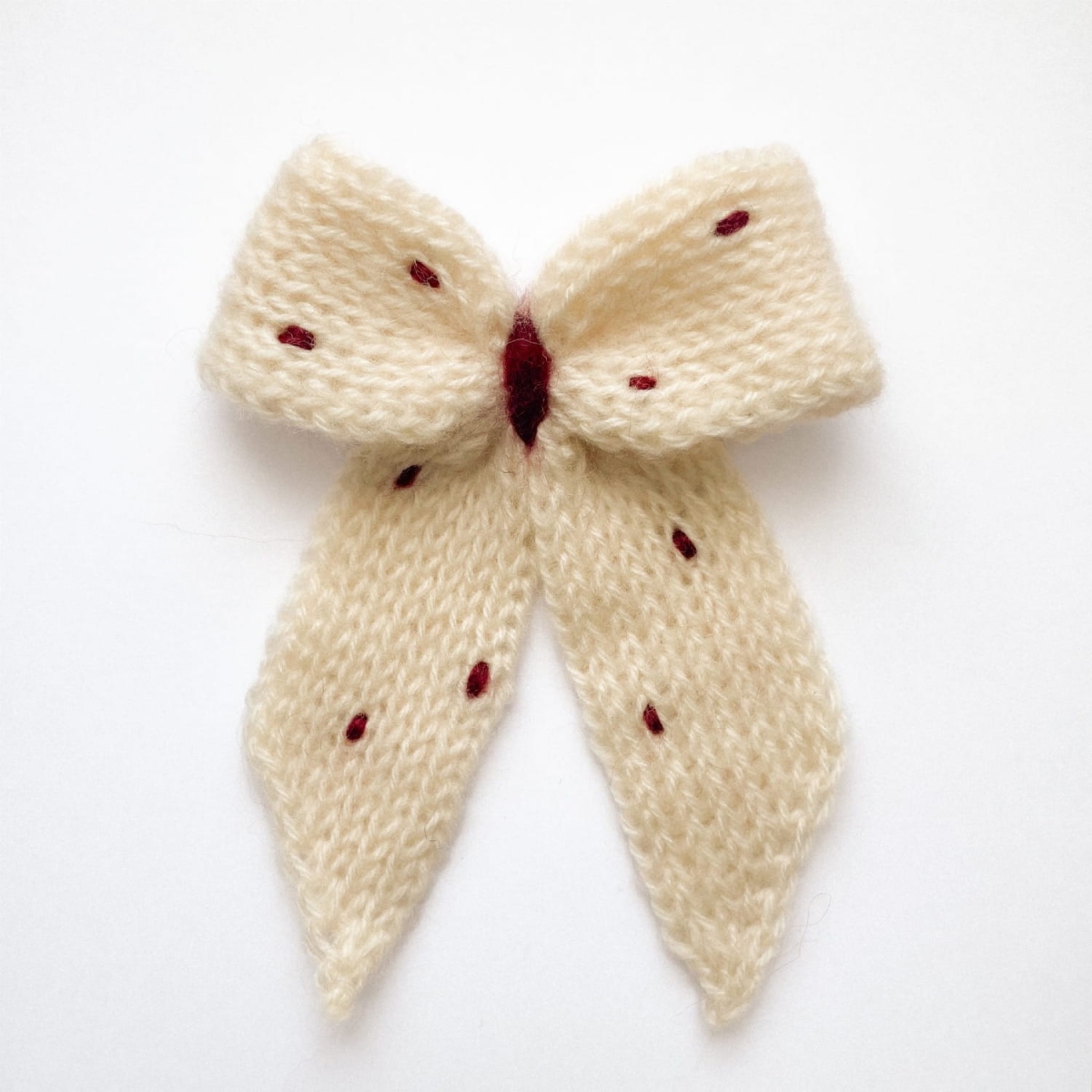 Ręcznie dziergana spinka do włosów w formie kokardy, widok z góry na jasnym tle.