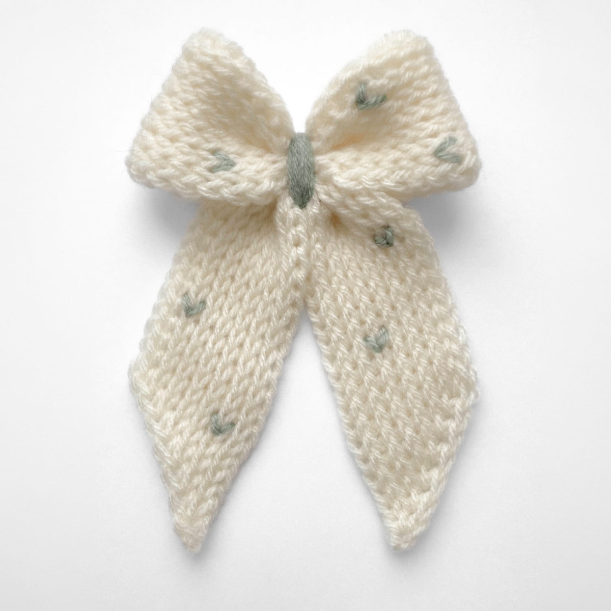 Ręcznie dziergana spinka do włosów w formie kokardy, widok z góry na jasnym tle.