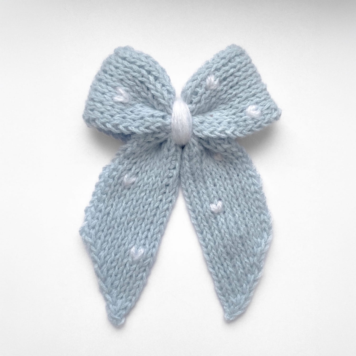 Ręcznie dziergana spinka do włosów w formie kokardy, widok z góry na jasnym tle.