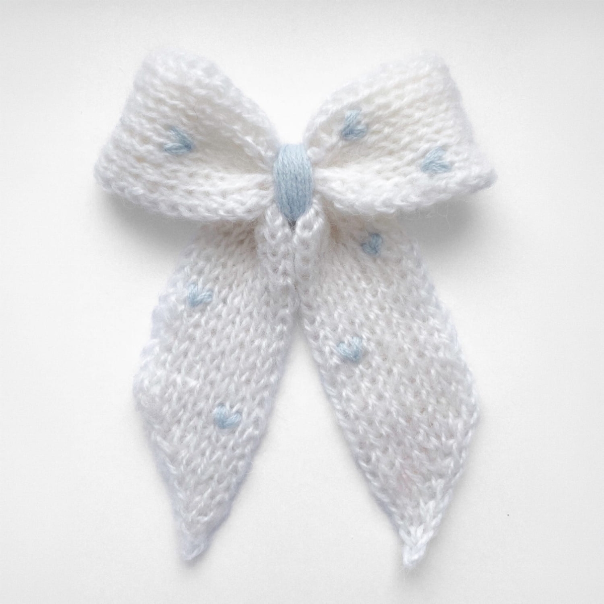 Ręcznie dziergana spinka do włosów w formie kokardy, widok z góry na jasnym tle.