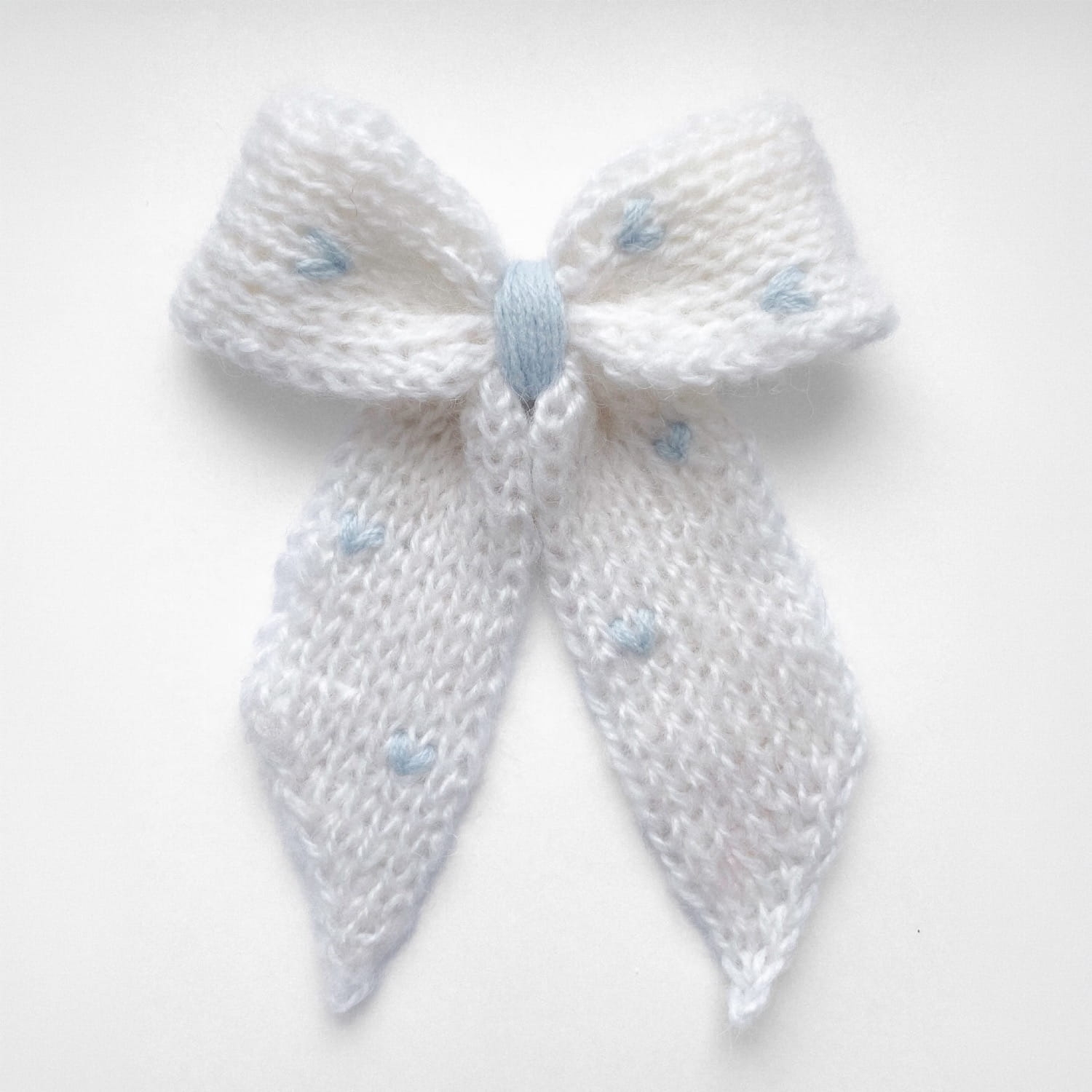 Ręcznie dziergana spinka do włosów w formie kokardy, widok z góry na jasnym tle.