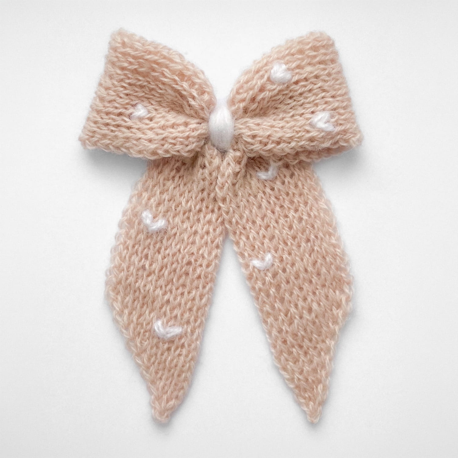 Ręcznie dziergana spinka do włosów w formie kokardy, widok z góry na jasnym tle.